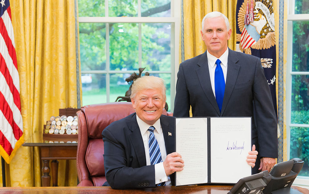Donald Trump In The Oval Office Holding Up A White Paper With Next To Him Standing Up Is Mike Pence