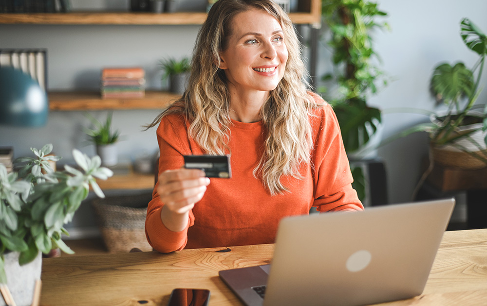 Mature woman sitting on lounge with credit card and laptop ready to buy something online